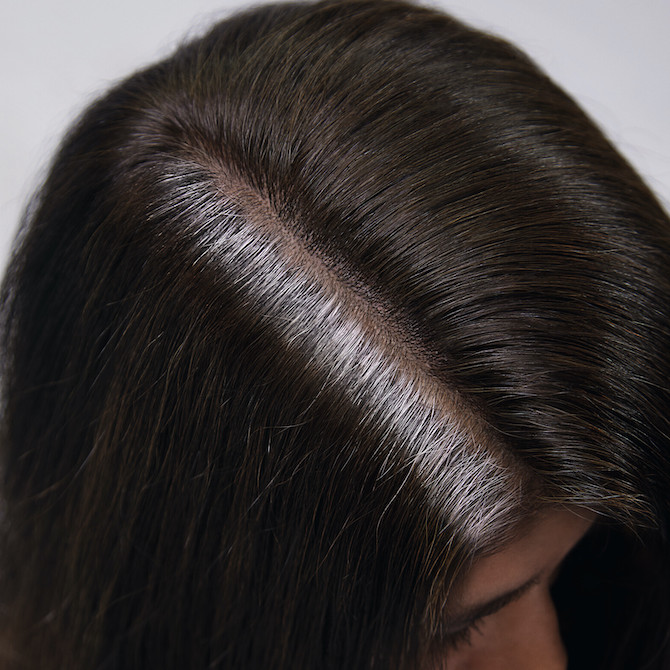 Top of woman’s head with brunette hair and stubborn gray roots.