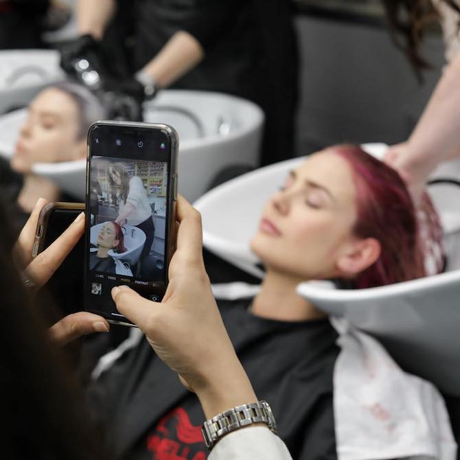 Hairdresser using a phone to take a photo of a woman having her hair washed.