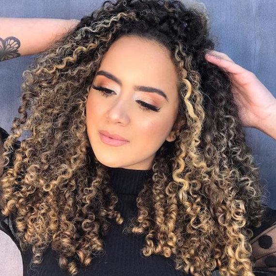 Frau mit blonden Strähnen im lockigen Haar, kreiert mit Wella Professionals.