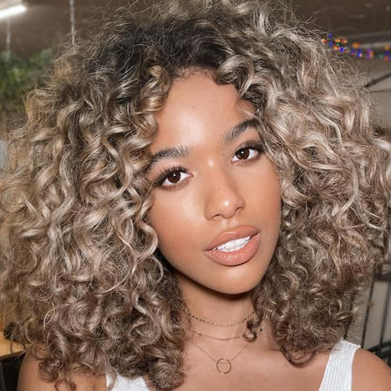 Eine Frau blickt in die Kamera, mit lockigem, beige-blondem Haar, kreiert mit Wella Professionals.