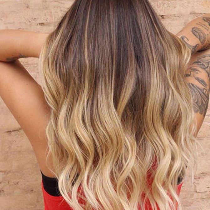 Woman with long golden blonde hair wit dark roots, styled with loose waves