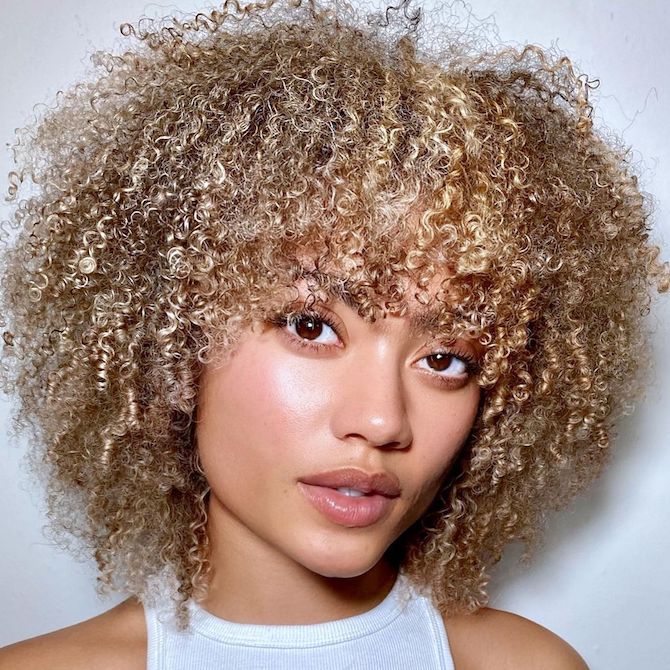 Model faces the camera with short, curly, sandy blonde hair and bangs.