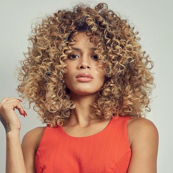 Woman facing the camera with curly, caramel blonde hair, created using Wella Professionals