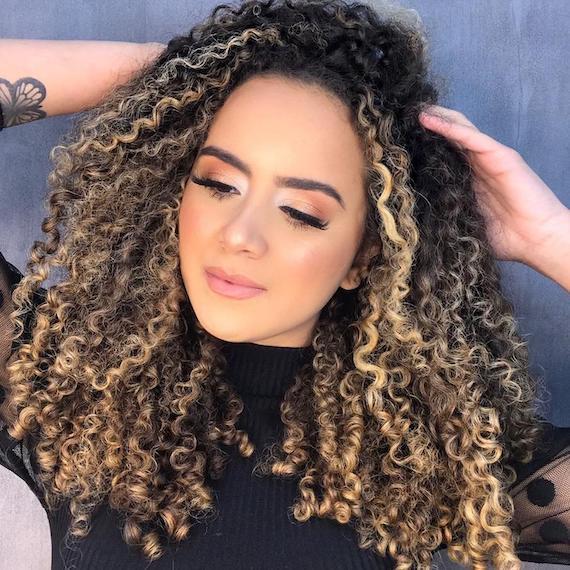 Woman with twilighting highlighting through curly hair, created using Wella Professionals.