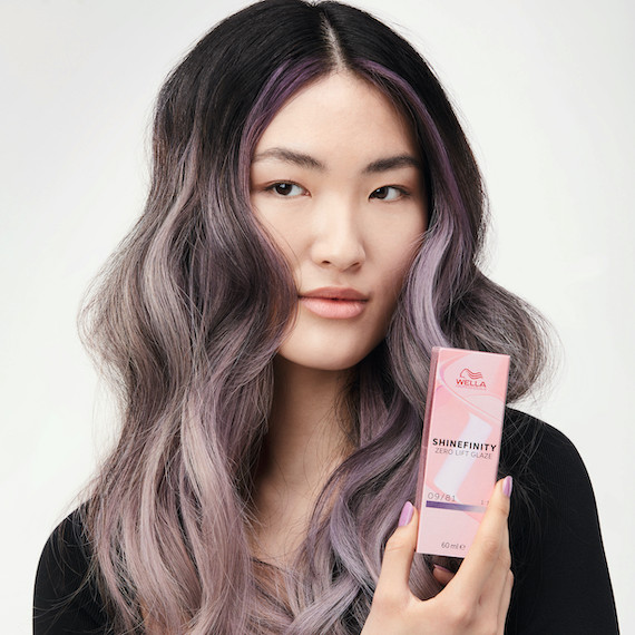 Model with dark hair and violet-blonde ends holds a box of Shinefinity by Wella Professionals
