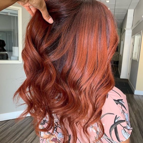 Model with wavy russet red hair and auburn lowlights.