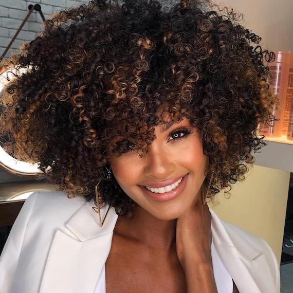 Woman smiles at the camera with curly, iced caramel espresso hair color.