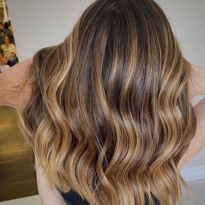 Back of woman’s head with long, wavy brown hair and warm blonde twilights, created using Wella Professionals.