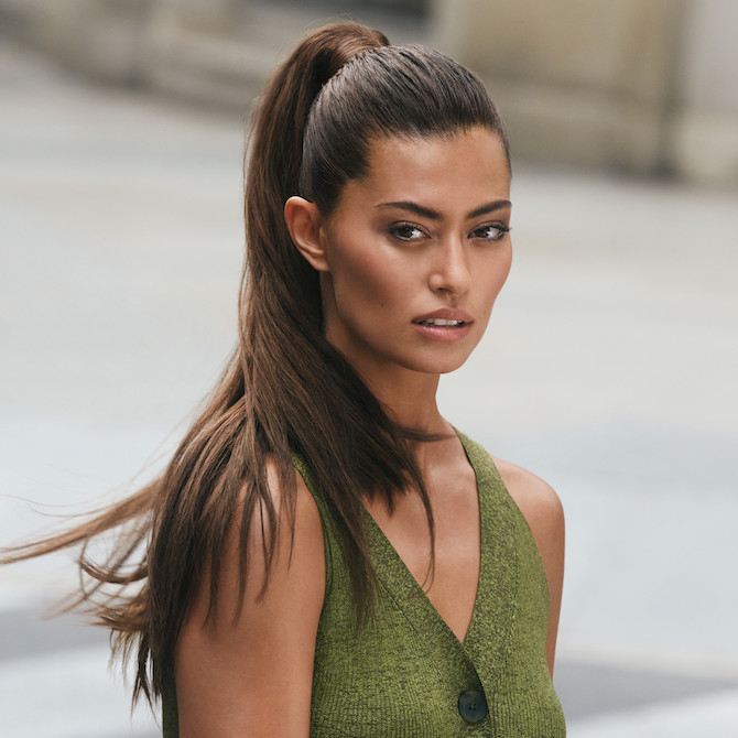 Model steht mit langen, braunen Haaren, die zu einem eleganten Pferdeschwanz gebunden sind, vor der Kamera.
