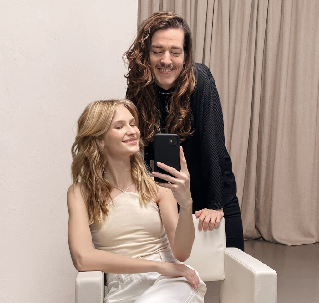 Kundin und Wella Frisör blicken lächelnd in die Smartphone Kamera.