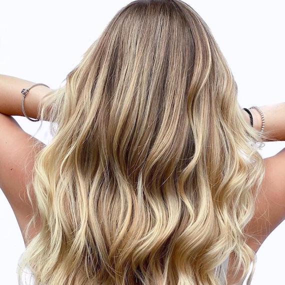 Hinterkopf einer Frau mit gewelltem, strandblondem Haar, kreiert mit Wella Professionals.