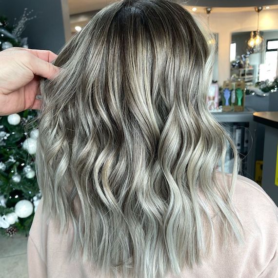 Back of woman’s head with mid-length, wavy, blonde and ash green hair, created using Wella Professionals.