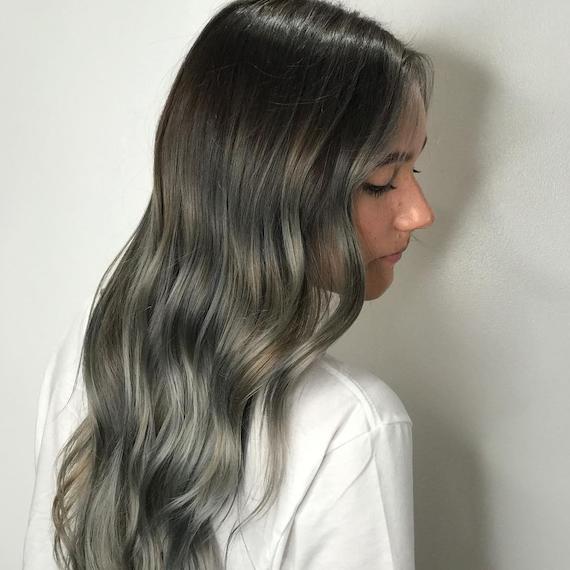 Side profile of woman with long, wavy, ash green-gray hair, created using Wella Professionals.