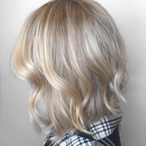 Seitenprofil einer Frau mit aschblondem Balayage-Bob, gestylt in lockeren Wellen, erstellt mit Wella Professionals.