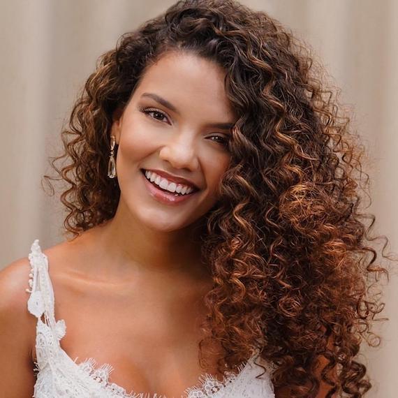 Frau mit langen brünetten Locken und Karamell-Balayage, kreiert mit Wella Professionals, sieht in eine Kamera.