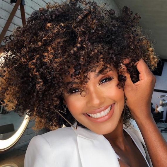 Frau mit lockigem, dunkelbraunem Haar und schokoladenfarbener Balayage, kreiert mit Wella Professionals, lächelt in die Kamera.