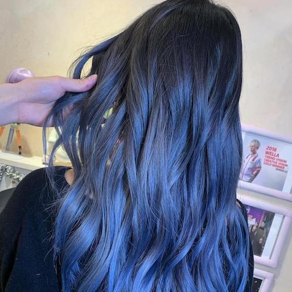Model with long, wavy hair and dark blue balayage, created using Wella Professionals.