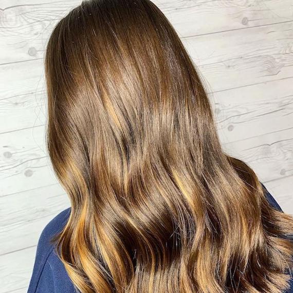Model with long, wavy hair and light brown balayage, created using Wella Professionals.