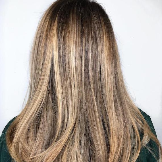 Back of woman’s head with dirty blonde balayage through straight hair, created using Wella Professionals.