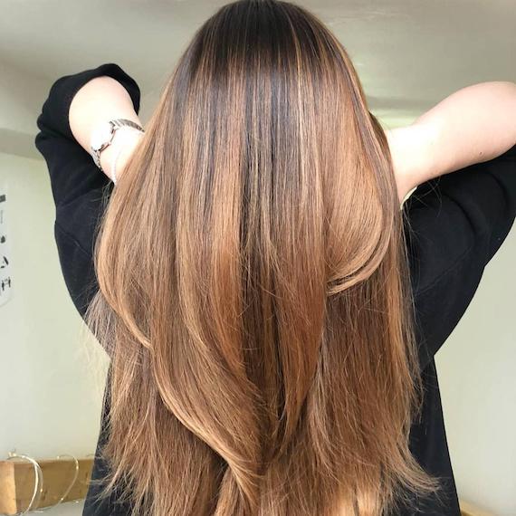 Back of woman’s head with golden brown balayage through straight hair, created using Wella Professionals.