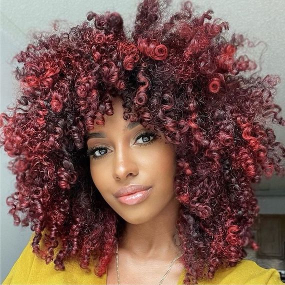Model with dark, curly hair and a cherry red balayage faces camera.