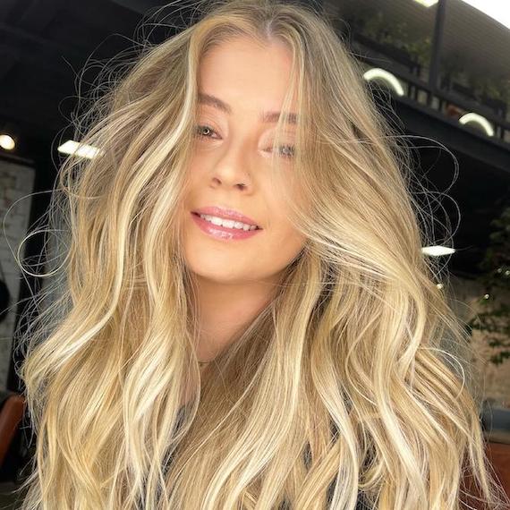 Woman facing camera with voluminous, beach blonde, wavy hair, created using Wella Professionals.
