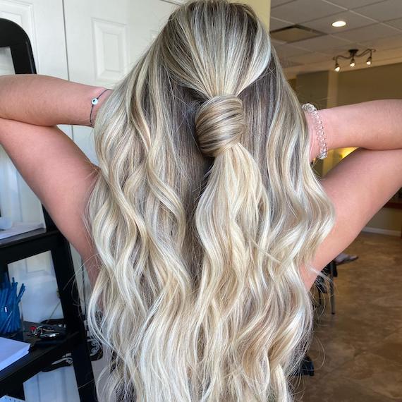 Back of woman’s head with long, beach blonde, tousled hair tied in a knot, created using Wella Professionals.