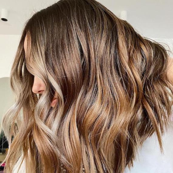 Side profile of woman with caramel brown, beachy, wavy hair, created using Wella Professionals.