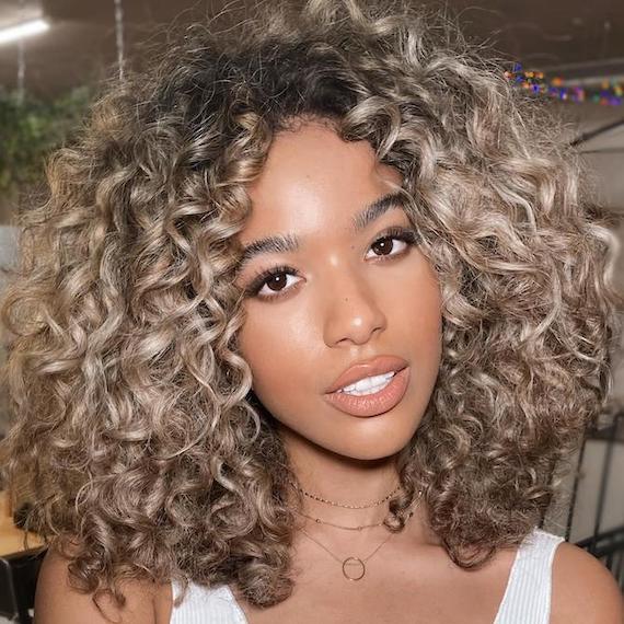 Woman facing camera with curly, beachy, beige blonde hair, created using Wella Professionals.