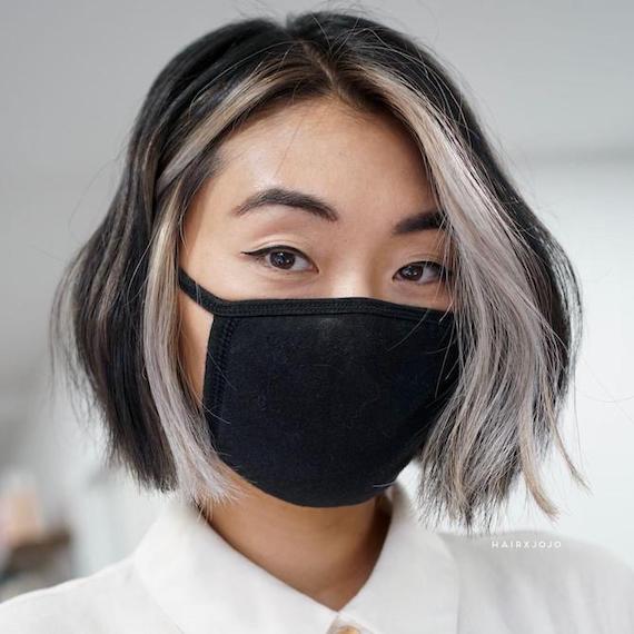 Woman facing the camera with a black face mask on. Her black and blonde hair is styled in a bob.