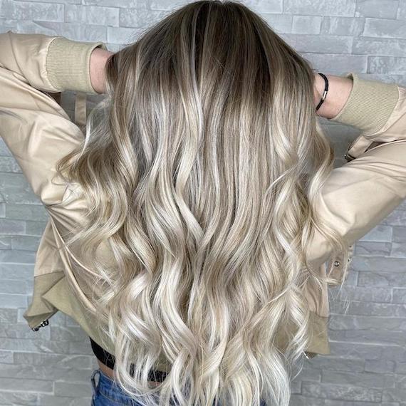 Back of woman’s head with long, loosely curled blonde hair and black roots, created using Wella Professionals.