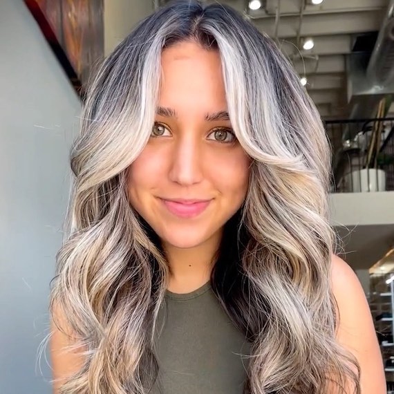 Modell mit schwarzem Ansatz und silberblonder Balayage, gestylt in lockeren Wellen.