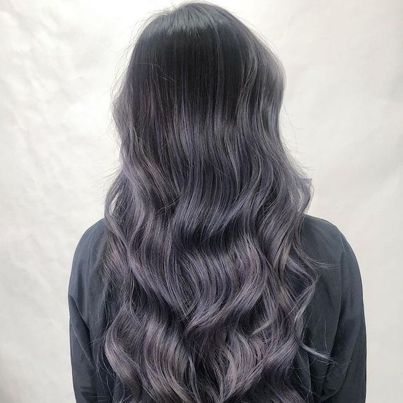 Hinterkopf des Modells mit langem, locker gelocktem, schwarzem Haar und lavendelfarbenem Balayage.