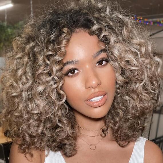 Frau mit dunklen Locken und blonden, chunky Highlights, kreiert mit Wella Professionals.