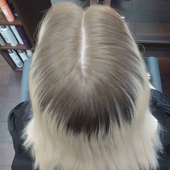 Foto von der Rückseite des Kopfes einer Frau mit blondem Haar und dunklen Ansätzen.
