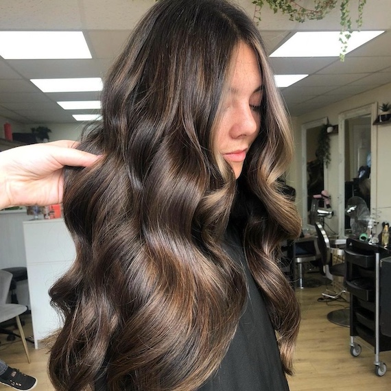 Side profile of model with very long, wavy, dark brown hair and caramel blonde highlights.