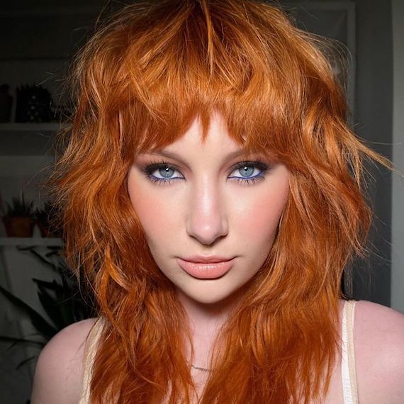 Model with red hair and shag haircut faces camera.