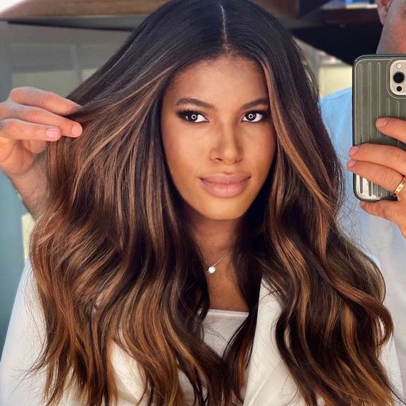 Model with long, wavy, dark brown hair and bronze highlights faces camera.