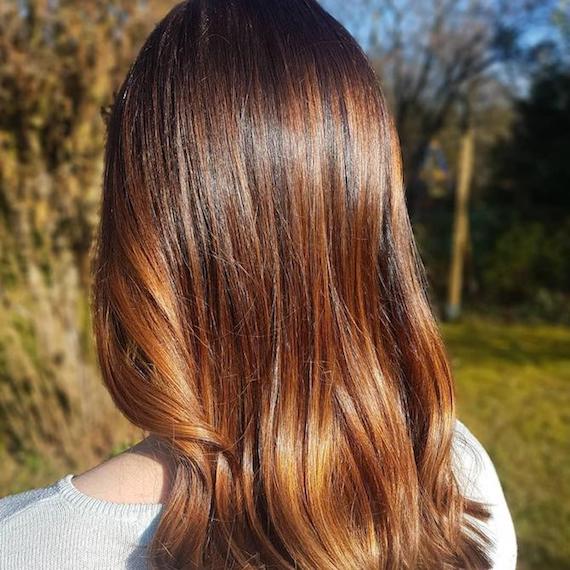 Close-up of a person's golden brown hair. They are facing away from the camera, looking out onto trees and greenery
