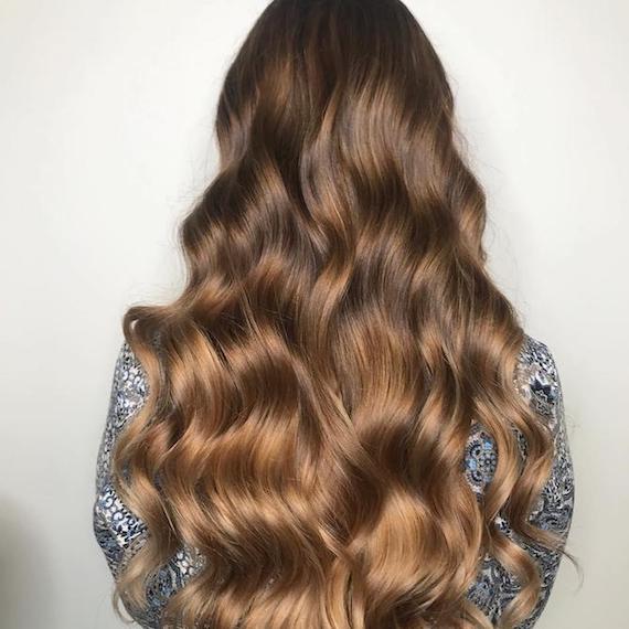 Back of model's head faces the camera. They have long, wavy brown hair.