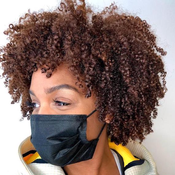 Frau mit Gesichtsmaske, deren lockiges kupferbraunes Haar mit Wella Professionals kreiert wurde.