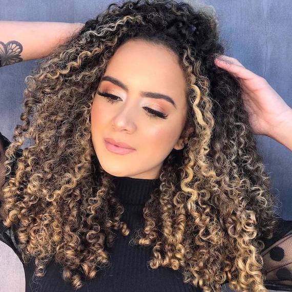 Frau mit dunkelbraunem lockigem Haar und blonden Strähnchen, kreiert mit Wella Professionals.