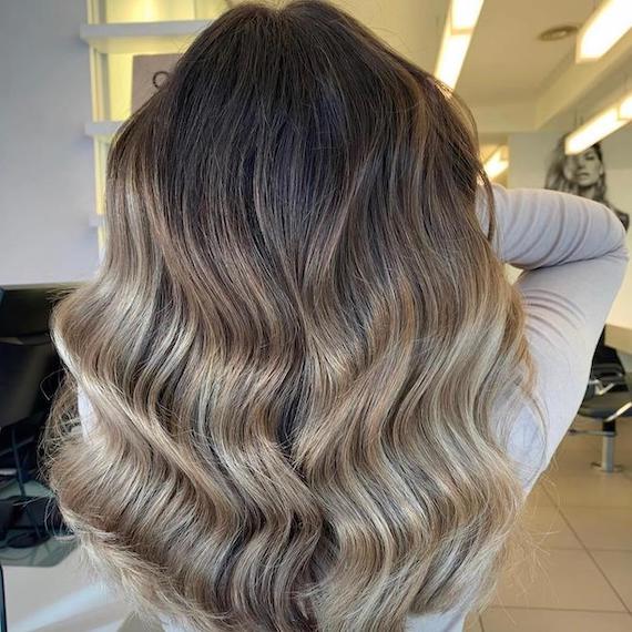 Hinterkopf einer Frau mit langem, gewelltem Haar und aschbrauner Balayage, kreiert mit Wella Professionals.