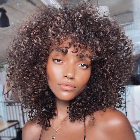 A model with very curly, ash brown hair and light brown eyes