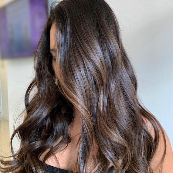 Frau mit langem, gewelltem, dunkelbraunem Haar und Balayage, kreiert mit Wella Professionals.