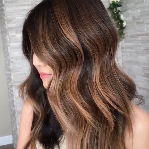 Model looks to the side. Their face is mostly concealed with their long, wavy iced cappuccino brown hair.