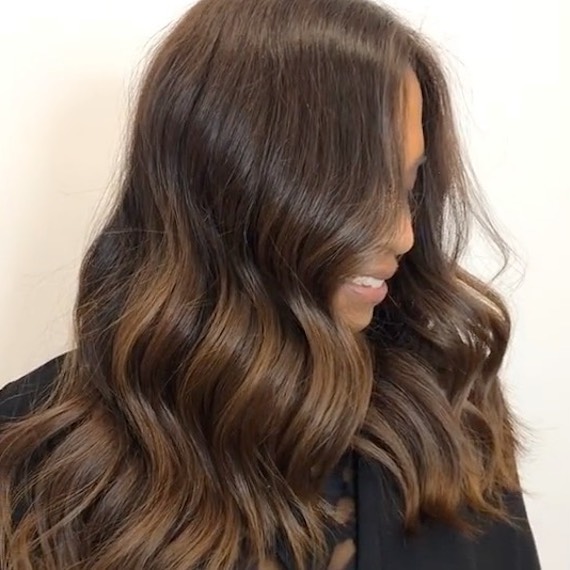 Model looks to the side and down so that their dark brown, wavy hair covers most of their face.