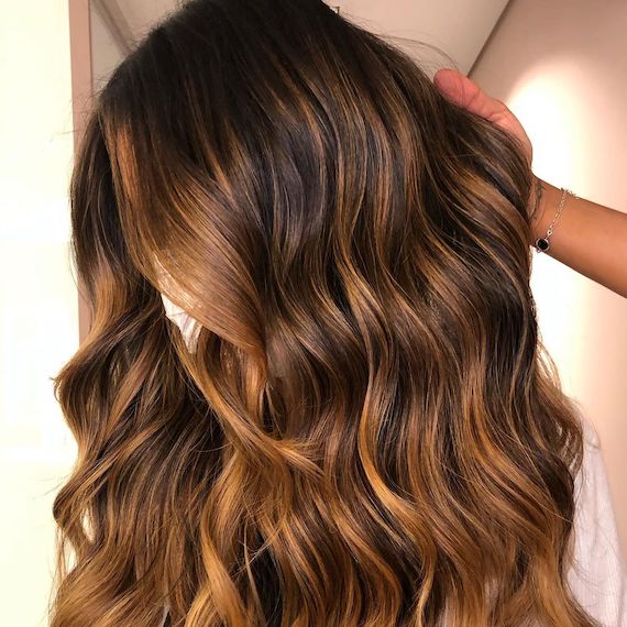 Close up of dark rooted wavy hair that’s been colored with cappuccino highlights.