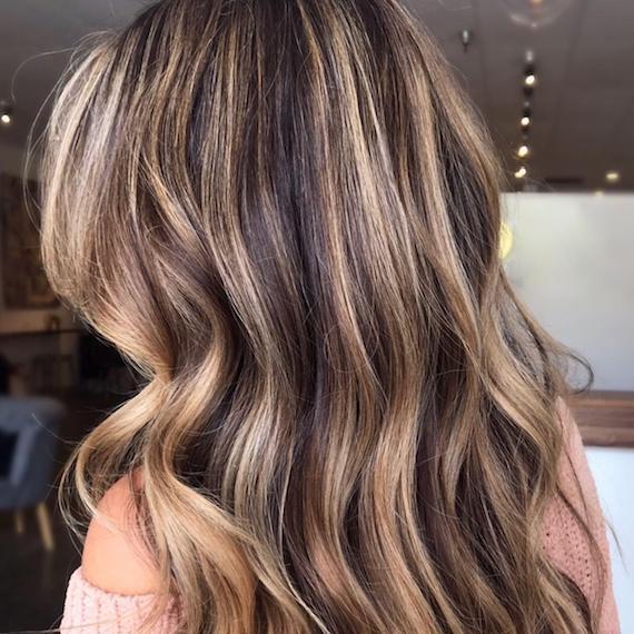 Back of woman’s head with long, wavy hair and caramel blonde highlights, created using Wella Professionals.