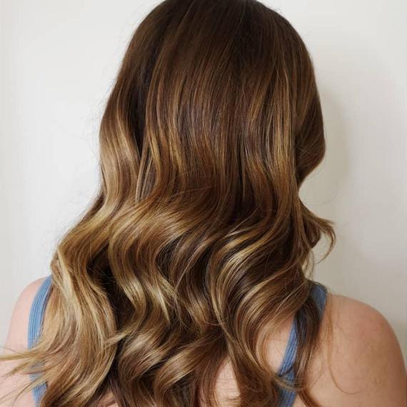 Hinterkopf einer Frau mit langem, leicht gewelltem Haar und karamellblonder Balayage, kreiert mit Wella Professionals.